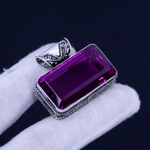 May include: A silver pendant with an ornate design features a large, rectangular, purple gemstone.