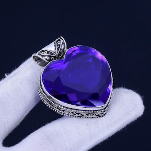 May include: A silver heart-shaped pendant with an ornate design and a large, faceted, purple gemstone.