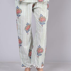 May include: Light green and white striped pajama pants with a floral pattern in shades of orange, pink, and blue. The pants have a pom-pom trim at the hem. The top of the pajama set is also visible.