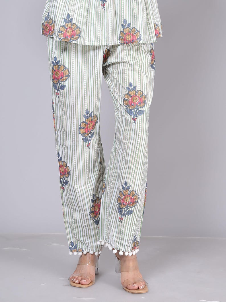 May include: Light green and white striped pajama pants with a floral pattern in shades of orange, pink, and blue. The pants have a pom-pom trim at the hem. The top of the pajama set is also visible.