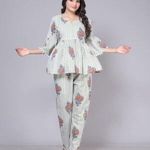 May include: A two-piece pajama set in a light green and white striped pattern. The top has a peplum design with floral accents and bell sleeves trimmed with white pom-poms. The matching pants also feature floral prints and pom-pom trim.