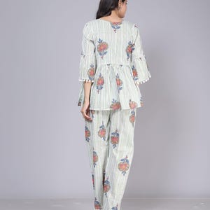 May include: A two-piece pajama set featuring a top and pants. The set is light green with vertical white stripes and a floral pattern in red, blue, and orange. The top has flared sleeves and a peplum, and the pants are straight-legged.