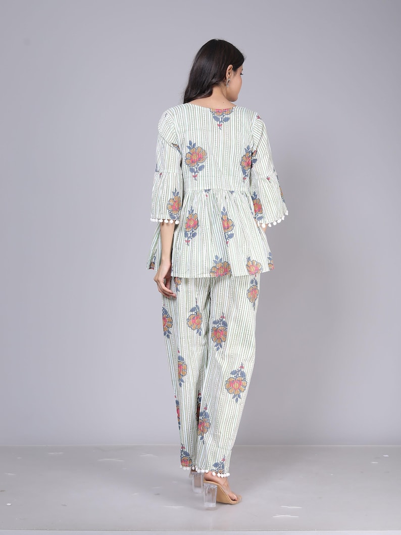 May include: A two-piece pajama set featuring a top and pants. The set is light green with vertical white stripes and a floral pattern in red, blue, and orange. The top has flared sleeves and a peplum, and the pants are straight-legged.