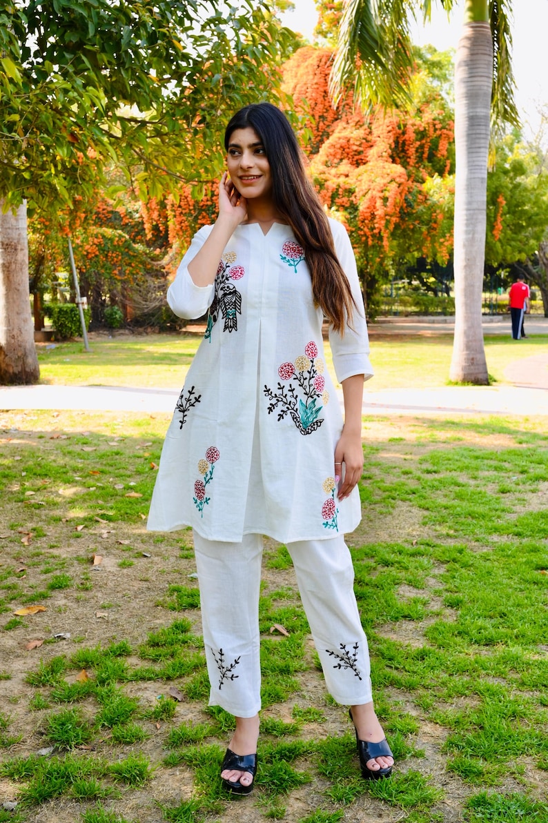 May include: White cotton kurta and palazzo set with floral embroidery. The kurta has a V-neck and three-quarter sleeves. The palazzo pants have a wide leg and are embroidered at the hem.