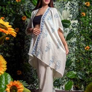 Könnte beinhalten: Cremefarbener Kimono mit offenem Schnitt und passende Hose mit blauen Musterelementen. Der Kimono hat ein sich wiederholendes blaues Design und einen geometrischen Rand. Das Outfit ist Teil eines koordinierten Sets, ideal für Freizeitkleidung.