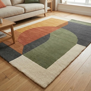 Könnte beinhalten: Rechteckiger Teppich mit geometrischem Muster. Das Design umfasst orange, grüne, graue und braune Formen, umrandet von einem cremefarbenen Rand. Der Teppich liegt auf einem Holzboden und passt in ein modernes Wohnzimmer.