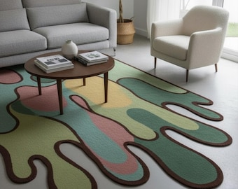 May include: A colorful area rug with an abstract design in shades of green, yellow, pink, and blue, outlined with a brown border. The rug is placed in a living room setting with a gray sofa, a white armchair, and a round coffee table.
