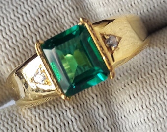May include: A gold ring with a large, square, emerald green gemstone and two smaller, round, clear gemstones.