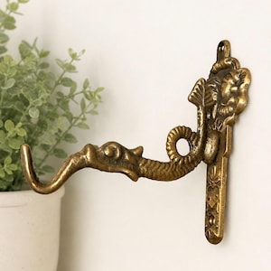 May include: A wall-mounted brass hook featuring a detailed dragon design. The hook extends outward with a curved, serpent-like body and a dragon head at the tip. The mounting plate is vertical and rectangular with embossed floral patterns.