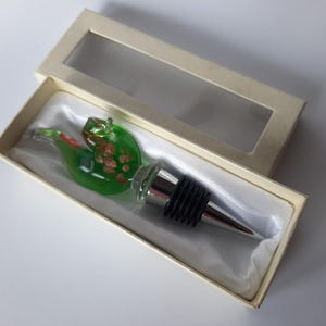 May include: A green glass bottle stopper with a silver top and a black rubber seal. The stopper is shaped like a bird with gold accents. The stopper is in a white box with a clear plastic window.