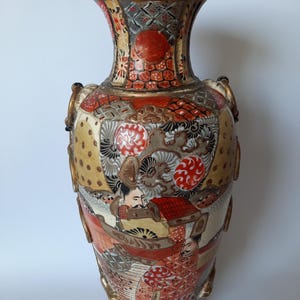 Könnte beinhalten: Eine verzierte Vase mit breiter Öffnung und bauchigem Körper. Sie hat einen goldenen Rand und Griffe, mit detaillierten Illustrationen in Rot, Gold und Creme. Das Design umfasst Figuren und geometrische Muster, was eine Vintage-Ästhetik erzeugt.