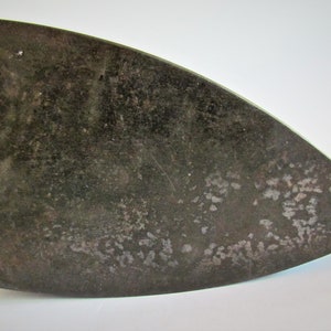 May include: A vintage cast iron flat iron with a dark gray finish and a slightly curved shape. The iron has a worn surface with visible signs of use.