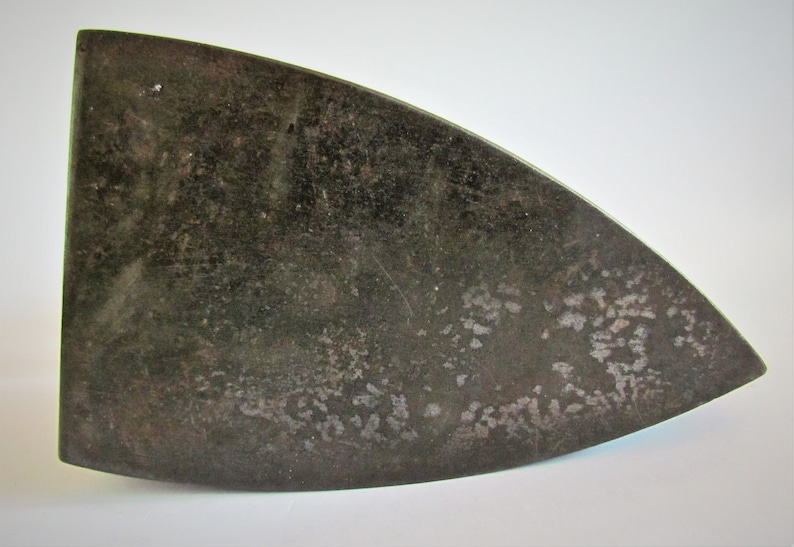May include: A vintage cast iron flat iron with a dark gray finish and a slightly curved shape. The iron has a worn surface with visible signs of use.