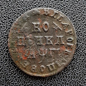 Könnte beinhalten: Nahaufnahme einer Kupfermünze mit der Inschrift "ПО ЖЕКД" in kyrillischer Schrift. Die Münze ist abgenutzt und hat eine rotbraune Patina.