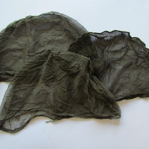 Op de afbeelding: Drie stukken groen gaas van stof, gekreukt en op elkaar gelegd. Het gaas is dun en doorschijnend, met een licht ruwe textuur.