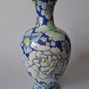 May include: A blue cloisonné vase featuring a repeating pattern of white and light blue flowers with yellow centers. The vase has a flared neck and a base rimmed with a metallic gold-toned finish, showcasing intricate enamel floral detailing.