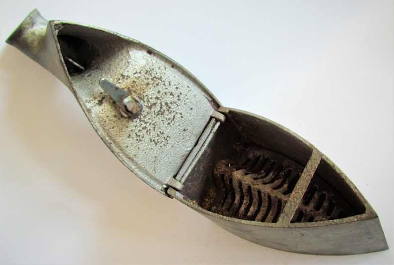 May include: A vintage cast iron flat iron with a hinged lid and a grate inside. The iron is silver in color and has a worn, aged appearance.