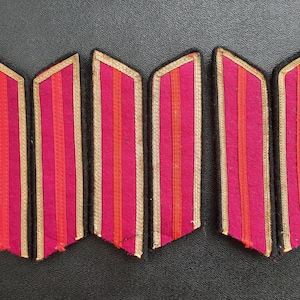 May include: Six vintage military uniform shoulder boards. Each board features a vibrant pink background with vertical orange and gold stripes. The edges are trimmed with gold braid, and the boards are set against a dark background.