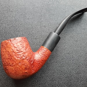 May include: A brown and black briar pipe with a rustic finish. The pipe has a curved stem and a bowl with a textured surface.