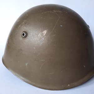 May include: A vintage olive drab helmet with a rounded shape. The helmet has two small circular vents and shows signs of wear, including scratches and scuffs. The helmet is likely made of metal and is a military or industrial item.