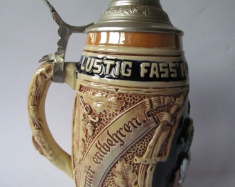 May include: A brown and tan ceramic beer stein with a silver lid. The stein has a handle shaped like a tree branch and features a scene of a man in a forest with the text "Lustig Fass'l" and "Immer erlaehgren".