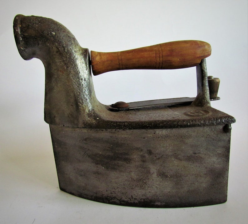 May include: A vintage cast iron flat iron with a wooden handle. The iron has a long spout on the side and is in a worn, aged condition.