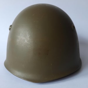 May include: A green military helmet with a rounded shape and two small metal rivets on the side.