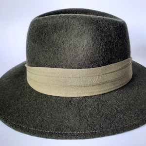 May include: A dark green fedora hat with a wide brim and a tan band. The hat is made of a soft, felt-like material. The hat's brim measures approximately 3 inches.