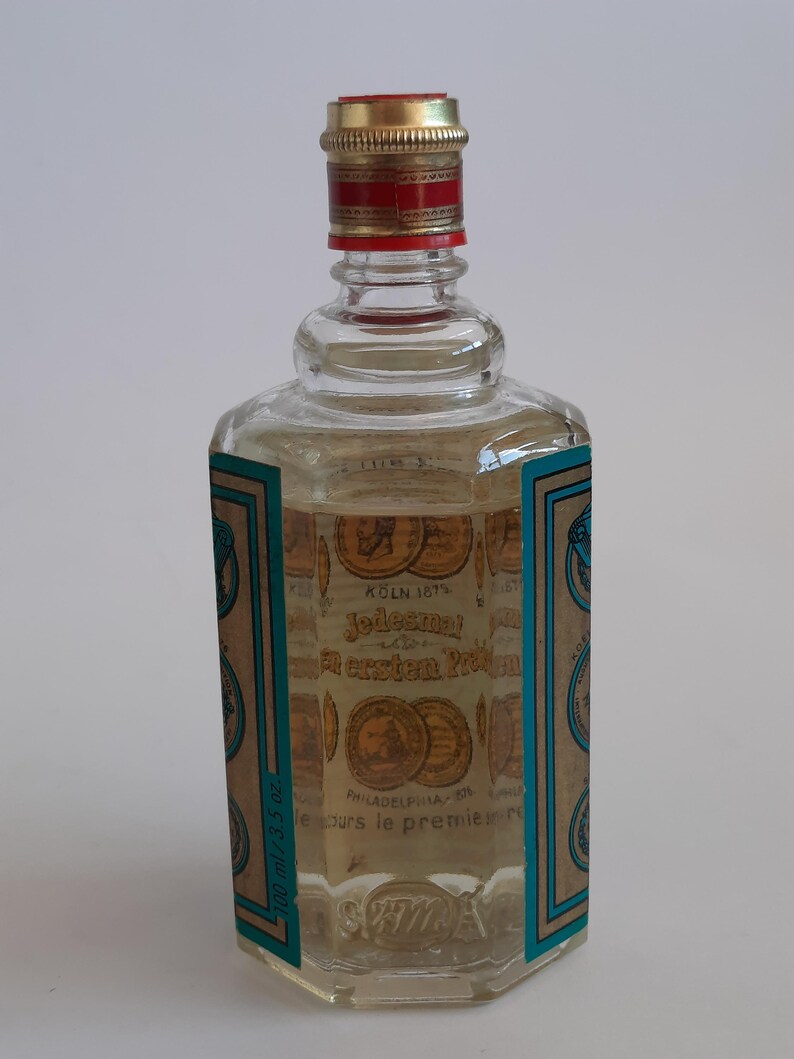Puede incluir: Una botella de vidrio transparente con una tapa dorada y roja. La botella tiene una etiqueta con texto e ilustraciones de monedas. El l&iacute;quido en el interior es de color amarillo claro. La botella est&aacute; etiquetada como "K&Ouml;LN 187".