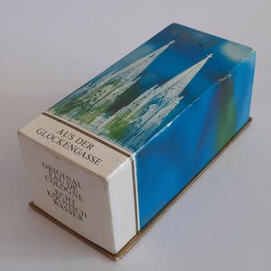 Puede incluir: Caja de colonia vintage con un dise&ntilde;o azul y verde que representa una catedral. La caja tiene texto en alem&aacute;n, incluyendo "Aus der Glockengasse" y "Original Eau de Cologne". La caja rectangular tiene una base dorada.