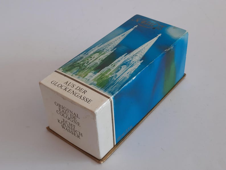 Puede incluir: Caja de colonia vintage con un dise&ntilde;o azul y verde que representa una catedral. La caja tiene texto en alem&aacute;n, incluyendo "Aus der Glockengasse" y "Original Eau de Cologne". La caja rectangular tiene una base dorada.