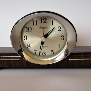 May include: A vintage black and silver clock with a wood base. The clock face has black numbers and a silver background. The clock is made by the company "Telechron".