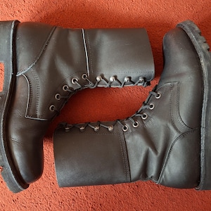 May include: A pair of black leather mid-calf boots featuring a lace-up front with silver-toned metal eyelets and hooks. The boots have a rounded toe, a thick lugged rubber sole, and visible stitching along the side panels and the heel counter.