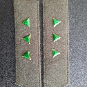 May include: Two dark green fabric shoulder boards with three green triangle-shaped insignia on each.