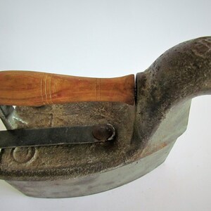 May include: A vintage cast iron charcoal iron with a wooden handle. The iron has a spout for adding fuel and a lever for adjusting the heat.