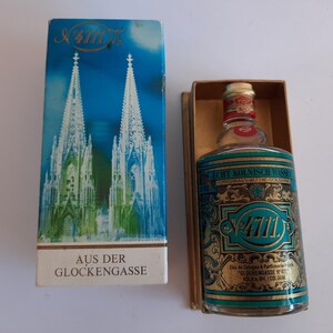 Puede incluir: Botella vintage de Eau de Cologne 4711 en su caja original. La botella es cil&iacute;ndrica con una etiqueta turquesa y dorada. La caja presenta un fondo azul con una representaci&oacute;n de una catedral. El texto "AUS DER GLOCKENGASSE" est&aacute; impreso.