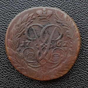 Könnte beinhalten: Eine Kupfermünze mit einer Krone und den Buchstaben "VP", die von einem Lorbeerkranz umgeben sind. Das Datum "1763" ist auf der Münze sichtbar.