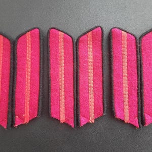 May include: Six red and black fabric patches with two thin red stripes on each. The patches are approximately 2 inches long and 1 inch wide.