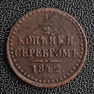 Puede incluir: Una moneda de color cobre con la inscripción "2 копейки серебромъ" y el año "1842" en ella.