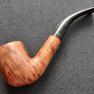 Pode incluir: Um cachimbo de tabaco curvo com uma tigela e haste de madeira. A tigela tem um padrão de grão em espiral castanho claro. A haste é cinza escuro e curva. O cachimbo tem o texto "S ROCK" na haste de madeira.