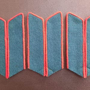 May include: Six dark green fabric patches with red trim. The patches are rectangular and have a slightly curved edge.