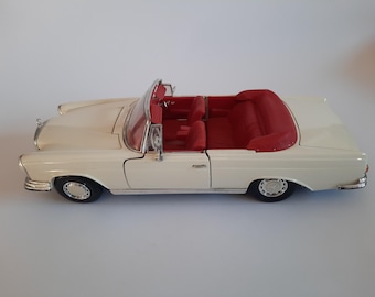 May include: Cream-colored convertible car model with a red interior. The model has detailed features, including chrome accents, black tires, and a classic design. The car is a vintage style, likely a collectible item.