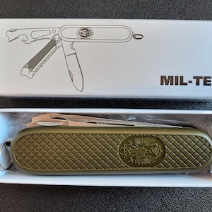 Puede incluir: Un cuchillo de bolsillo verde con un logotipo de MIL-TEC en el mango. El cuchillo está cerrado y tiene una variedad de herramientas, incluyendo un abridor de botellas, una sierra y un destornillador.