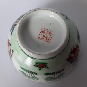 May include: An antique porcelain bowl with a light green exterior and a white interior. The bowl features colorful painted designs of flowers, birds, and other decorative elements. The bottom of the bowl has a red stamp.
