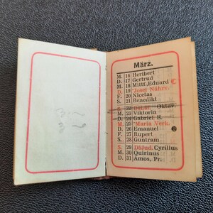 Puede incluir: Un peque&ntilde;o calendario vintage con un borde rojo. El calendario est&aacute; abierto al mes de marzo. Los d&iacute;as de la semana se abrevian como M, D, F y S. Los d&iacute;as del mes est&aacute;n numerados del 16 al 31. Cada d&iacute;a tiene un nombre asociado. El calendario est&aacute; impreso en tinta negra sobre papel blanco.