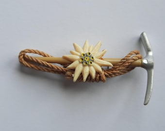 Puede incluir: Una cuerda marrón envuelta alrededor de un pico plateado con una flor de edelweiss de plástico blanco unida al mango.