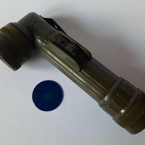 Op de afbeelding: Een groene zaklamp met een zwarte schakelaar en een blauwe lens. De zaklamp heeft een geribbeld lichaam en een handvat.