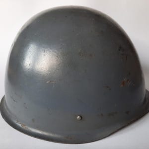 May include: A gray military helmet with a slightly worn finish. The helmet has a rounded shape and a smooth surface.