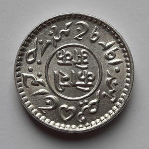 Può includere: Moneta d'argento con scrittura araba e il numero 26 sul bordo.