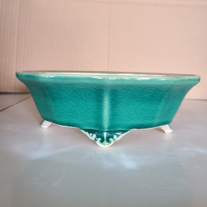 Op de afbeelding: Een groene keramische plantenpot met een getextureerd glazuur en vier decoratieve pootjes.